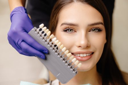 Dentist choosing teeth enamel shade color for young smiling female patient before whitening procedure.